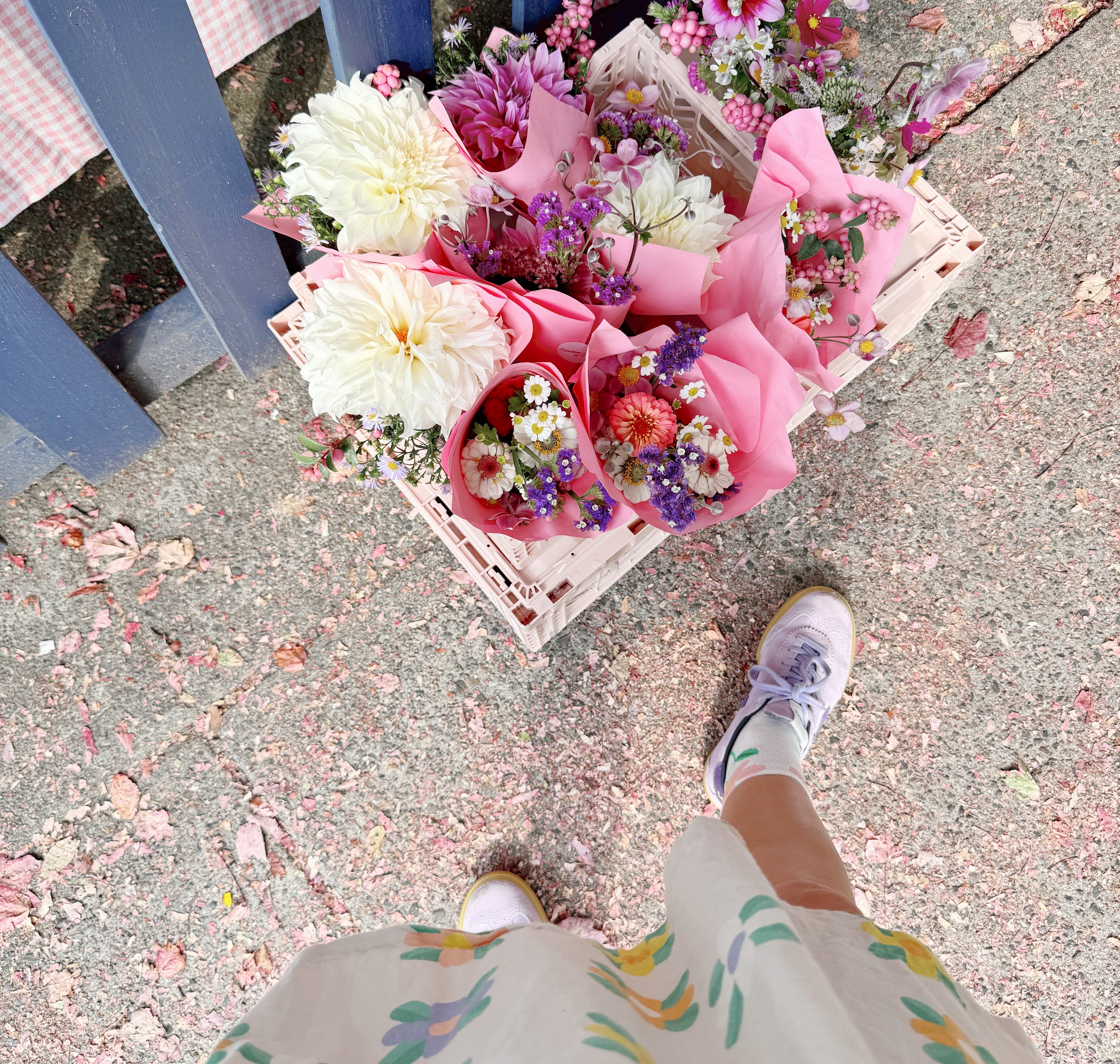 Bouquets of flowers on a sidewalk with a person wearing colorful shoes and a floral skirt.