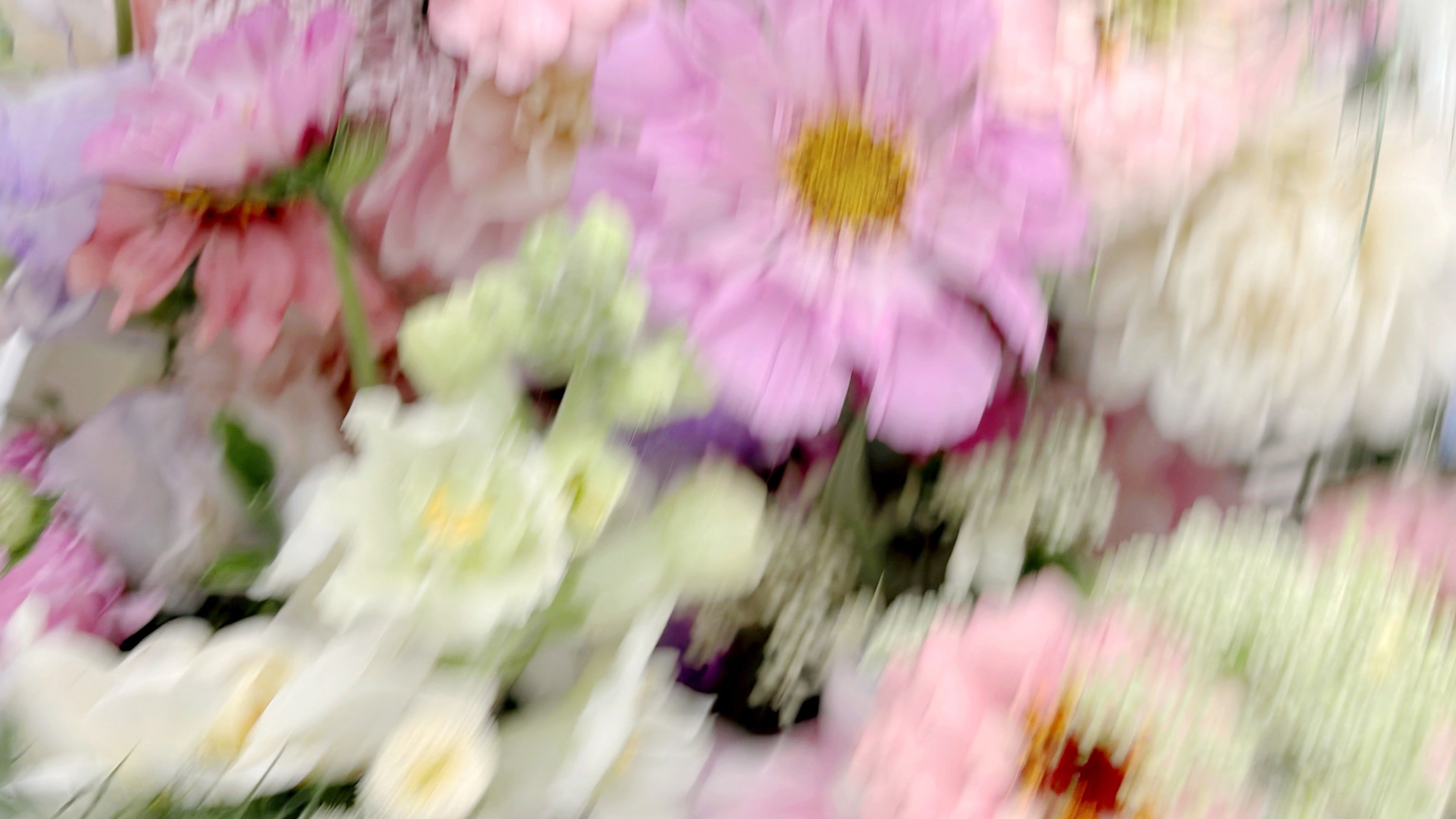 A close-up of a mixed floral arrangement featuring light pink, lavender, and white flowers with yellow centers and green foliage.